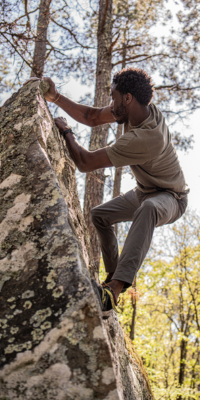 Man bouldering in a forest while wearing the rustic green Todra.