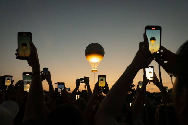 cellphones screens shows the hot-air balloon with the Olympic cauldron taking off in Paris, France