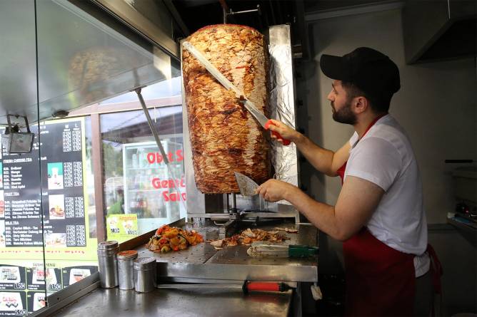 Worker shaving meat of vertical rotisserie.