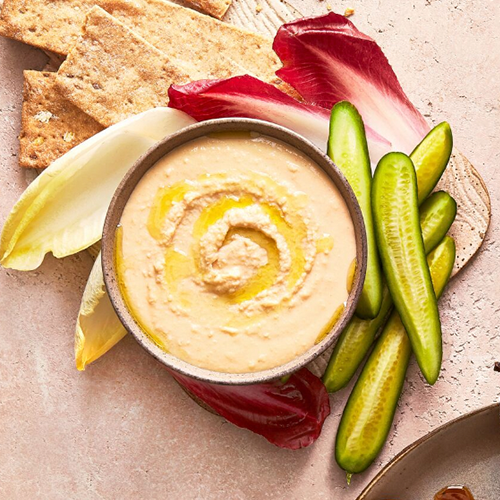 Red Lentil Hummus in a bowl with sliced vegetables and crackers on the side