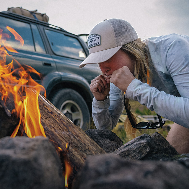 Woman crouching over a fire in PFG gear.