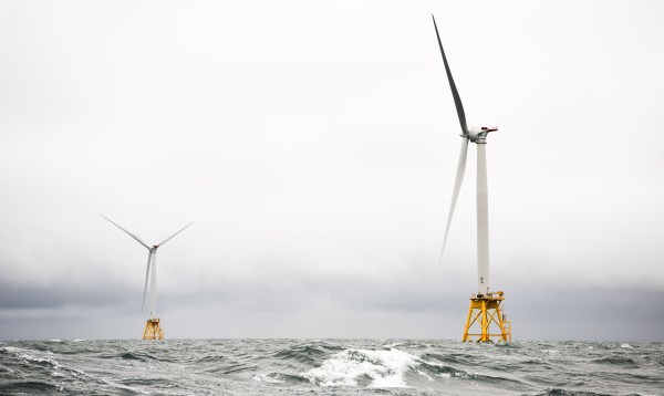 Two offshore wind turbines sit in grey churning water against a great sky