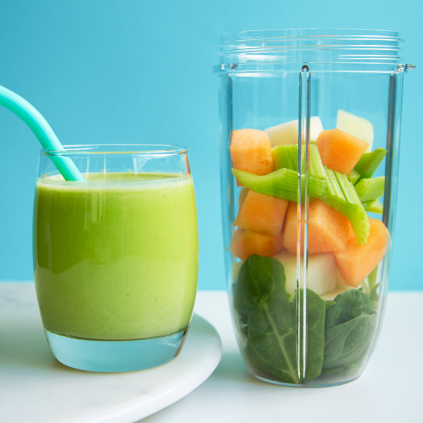 Melon smoothie next to pieces of fruits and vegetables in a cup