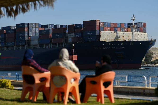 People watch as a ship transits the Suez Canal in the Red Sea