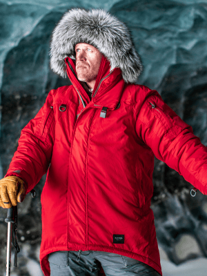 Man wearing the Red Allta Parka in an ice cave in Alaska. Has the hood up showing off the Coyote Ruff Fur Hood. Also wearing the Timber Guide Gloves