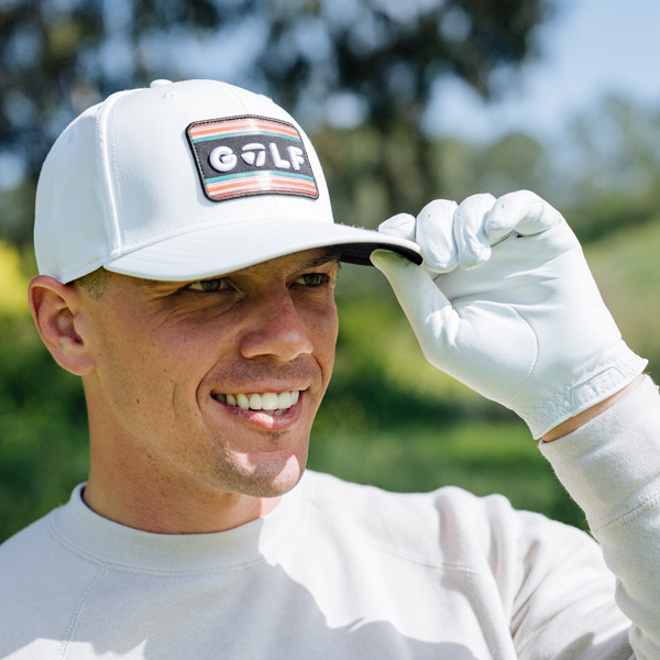 Male golfer wearing the white TaylorMade sunset golf snapback and a white TaylorMade Tour Preferred glove, smiling and grabbing the bill of his hat.