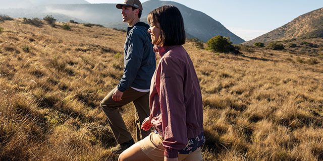 Two people hiking through a grassy, hilly, landscape.