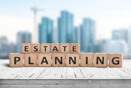 Blocks sitting on a wooden pier in front of skyscrapers have letters painted on them that read, "Estate planning"