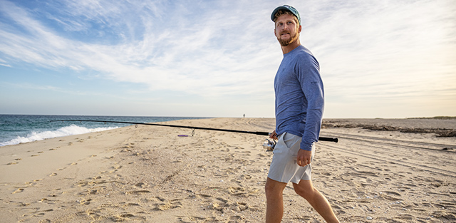 A man walking on the beach with a fishing pole.