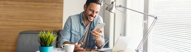 Man using his phone at his desk with a laptop.