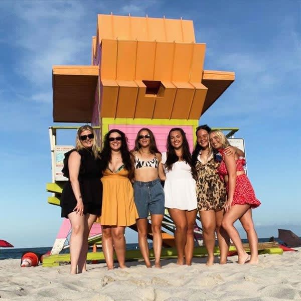 A group of women pose in front of a lifeguard stand on the beach