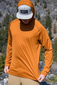 Man wearing the rust colored Geo-T while stretching to show how flexible and wearing the the hood over a hat