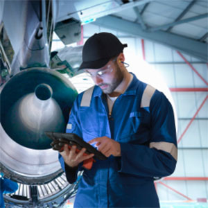 A chevron employee in a hat and goggles looks over an airplane's engine