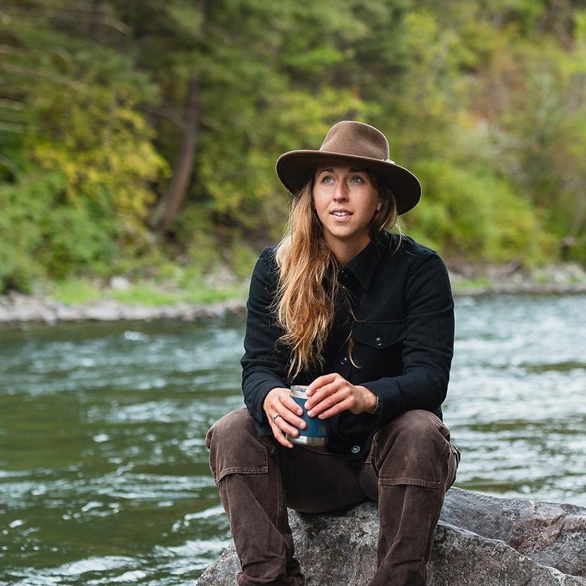 Woman sitting on a rock by the river wearing Duckworth button-up 