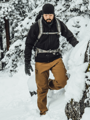 Man wearing the Black Testa Softshell Jacket and Coyote Testa Softshell Pants while hiking through the snow