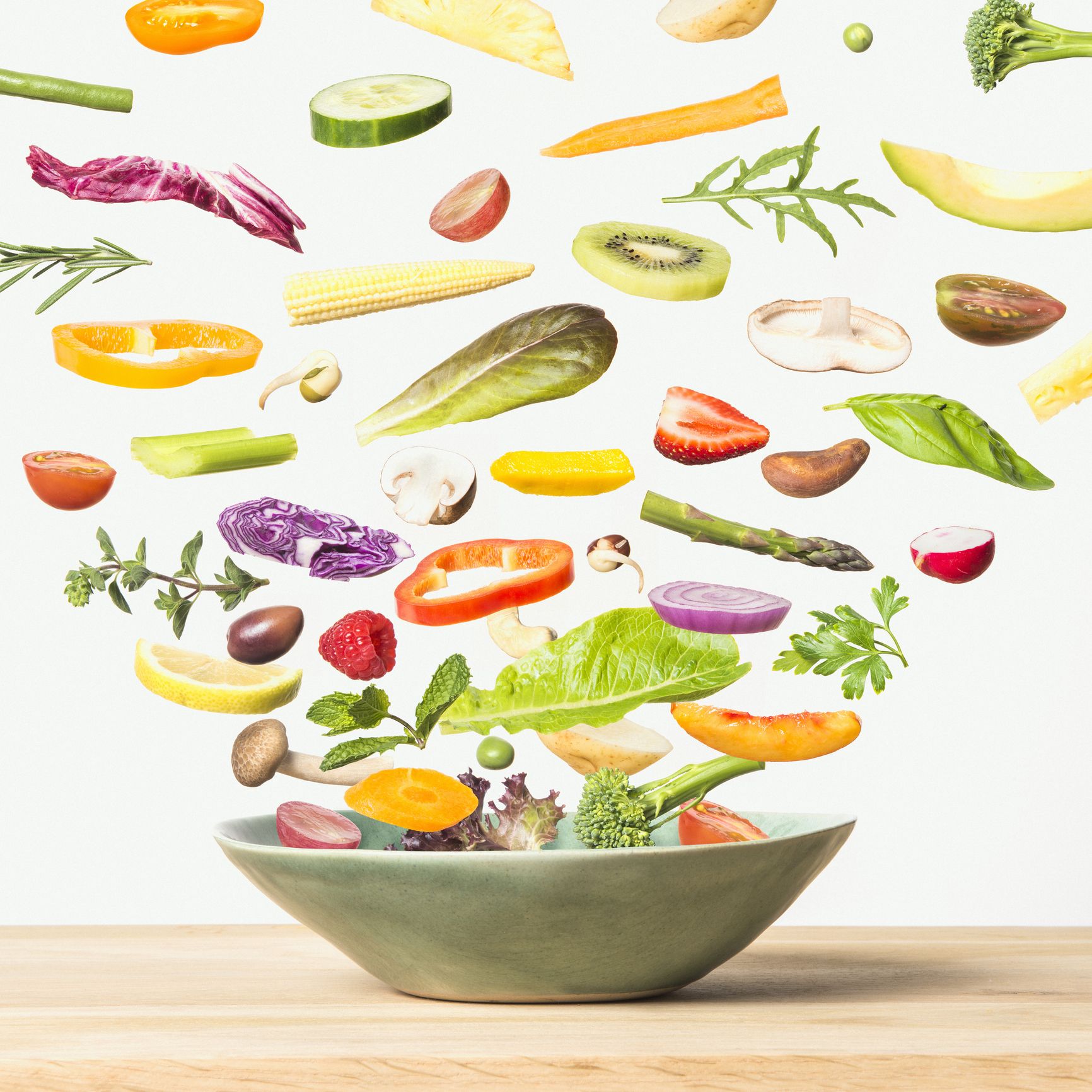 depiction of various fruits and vegetables falling into a green ceramic bowl