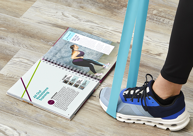 Woman with band under foot doing an exercise while looking at the Easy Resistance Band guide