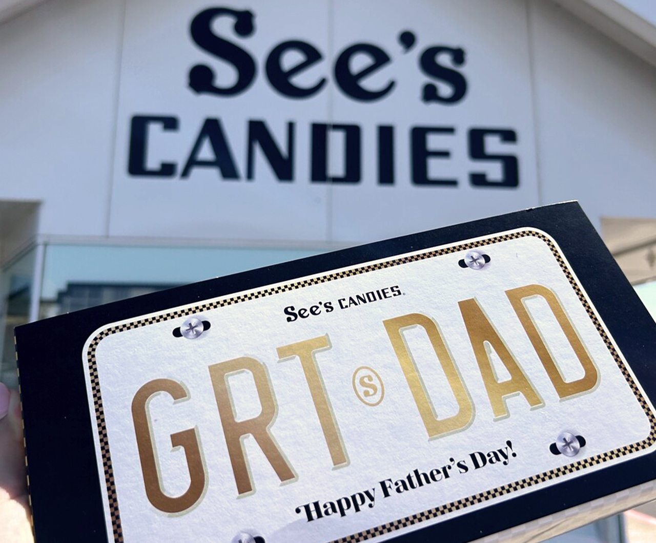 A Hand Holding a Father’s Day Box of Chocolates in Front of a See’s Candies Shop