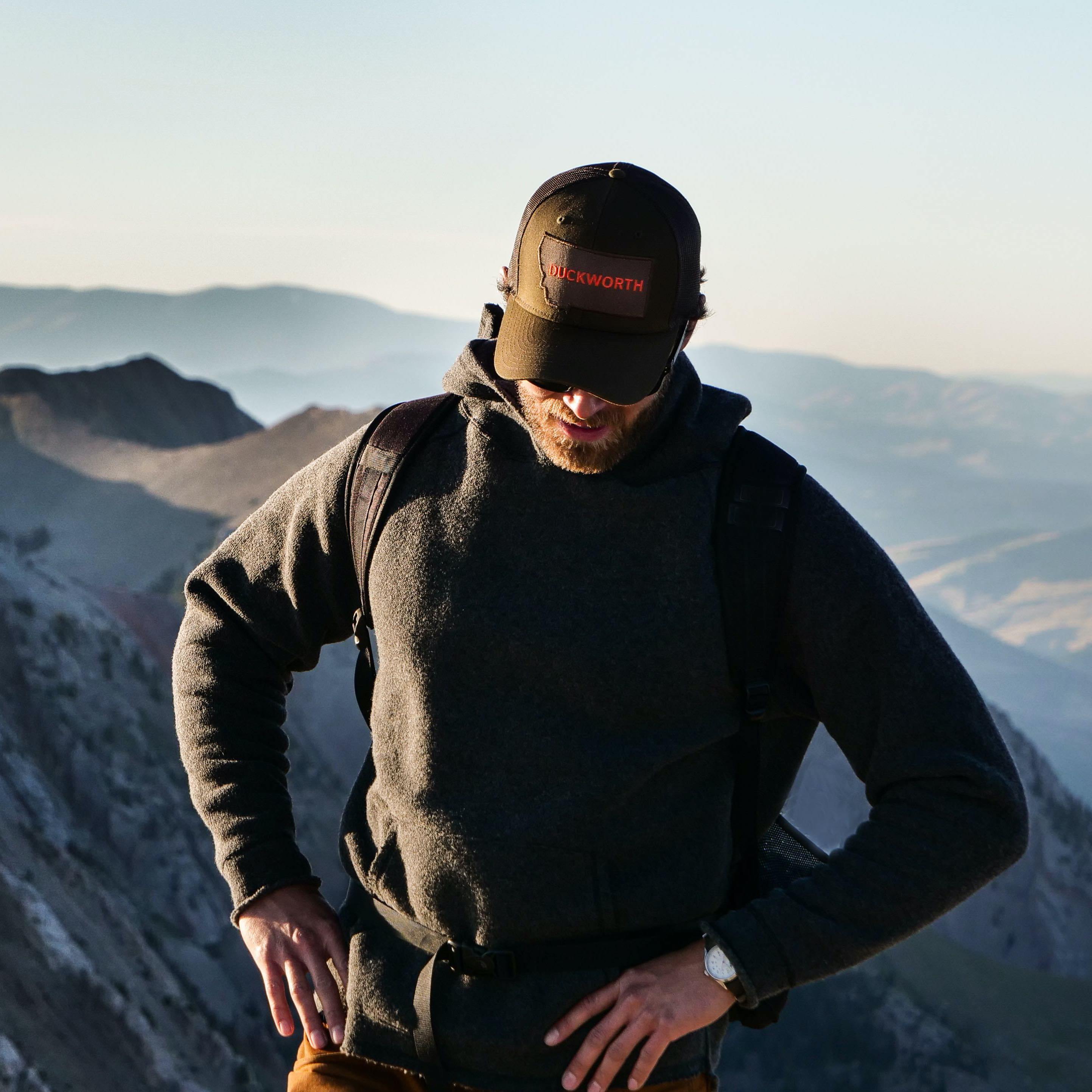 Man standing on top of mountain wearing a Duckworth hat and sweater