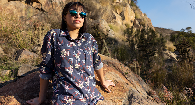 A woman in sunglasses and a floral hiking shirt enjoying the trail.