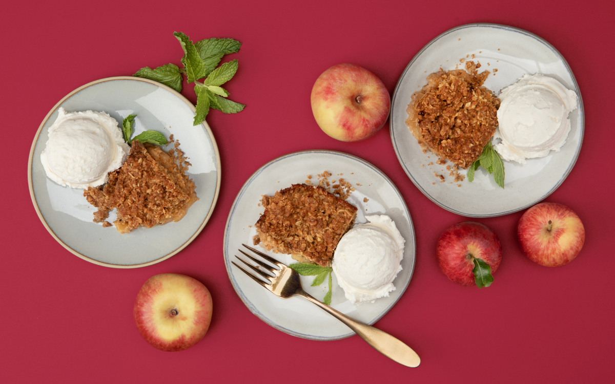 Overhead shot of three plates of apple crumble and vanilla ice cream with apples on the side. 