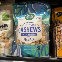 A bag of Whole Foods Market brand, Fairtrade organic cashews that have been dry roasted with sea salt sits on a shelf alongside other bags of cashews.