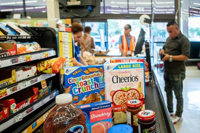 A conveyer belt of groceries at a checkout aisle and a man waiting to pay.