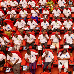 An aerial view of an auditorium with rows full of attendees each wearing white shirts embroidered with the Fairtrade logo.