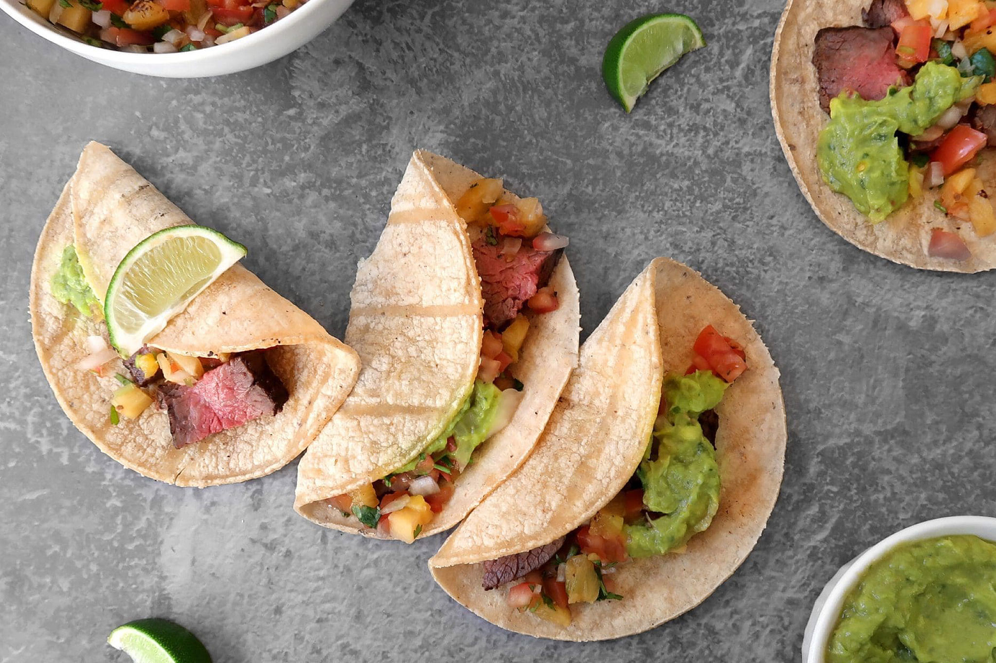 four tri-tip tacos topped with pineapple salsa, with lime and guacamole