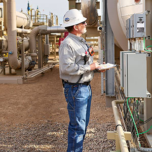 a chevron employee in a hard hat and goggles looking at a meter at a gas pipe