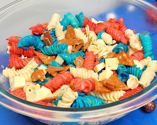 Blog idea: a glass bowl of pasta salad with cheese, pepperoni, and red, white, and blue noodles on a counter