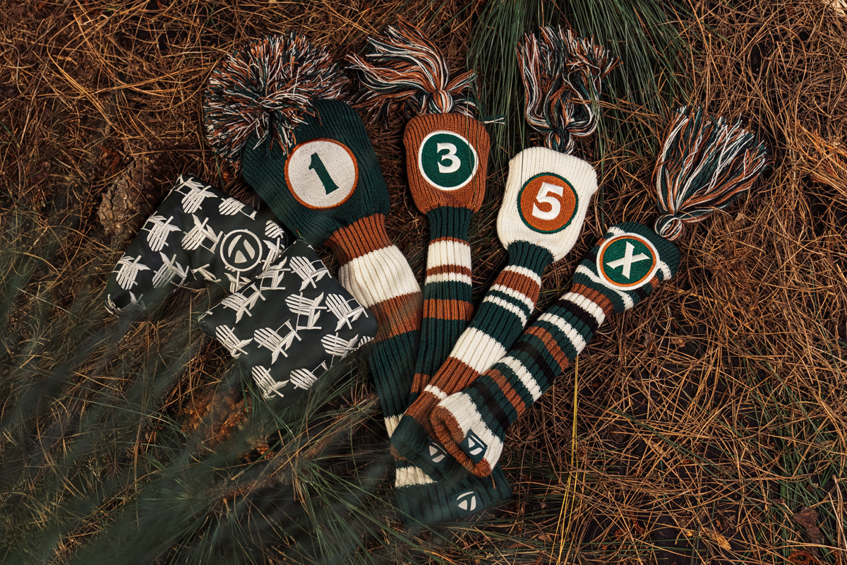 2024 Men's Summer Commemorative blade headcover, mallet headcover, driver headcover, 3 wood headcover, 5 wood headcover and rescue headcover laid out on the ground in the forest