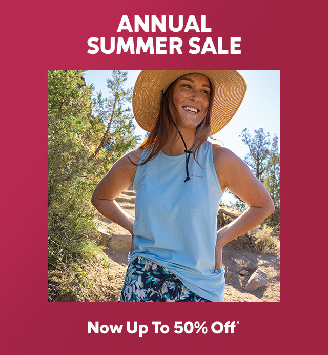 A woman stands on a trail smiling in a hat and a hiking shirt.