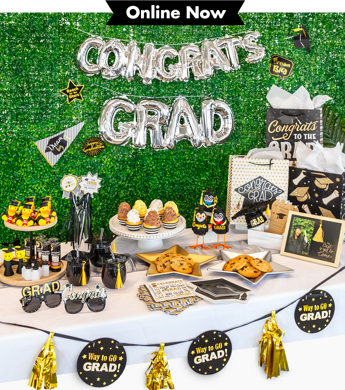 Variety of graduation-themed glasses, serveware, decorations, and snacks on a table with a silver balloon garland saying &#x22;congrats grad&#x22;