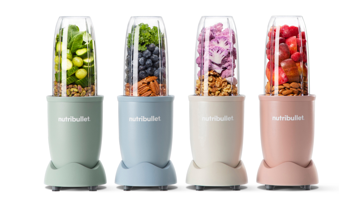 Four colorful nutribullet Pro blenders in a row filled with various nuts, fruits and veggies. 