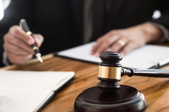 A judge is writing with a fountain pen at a desk that includes a gavel