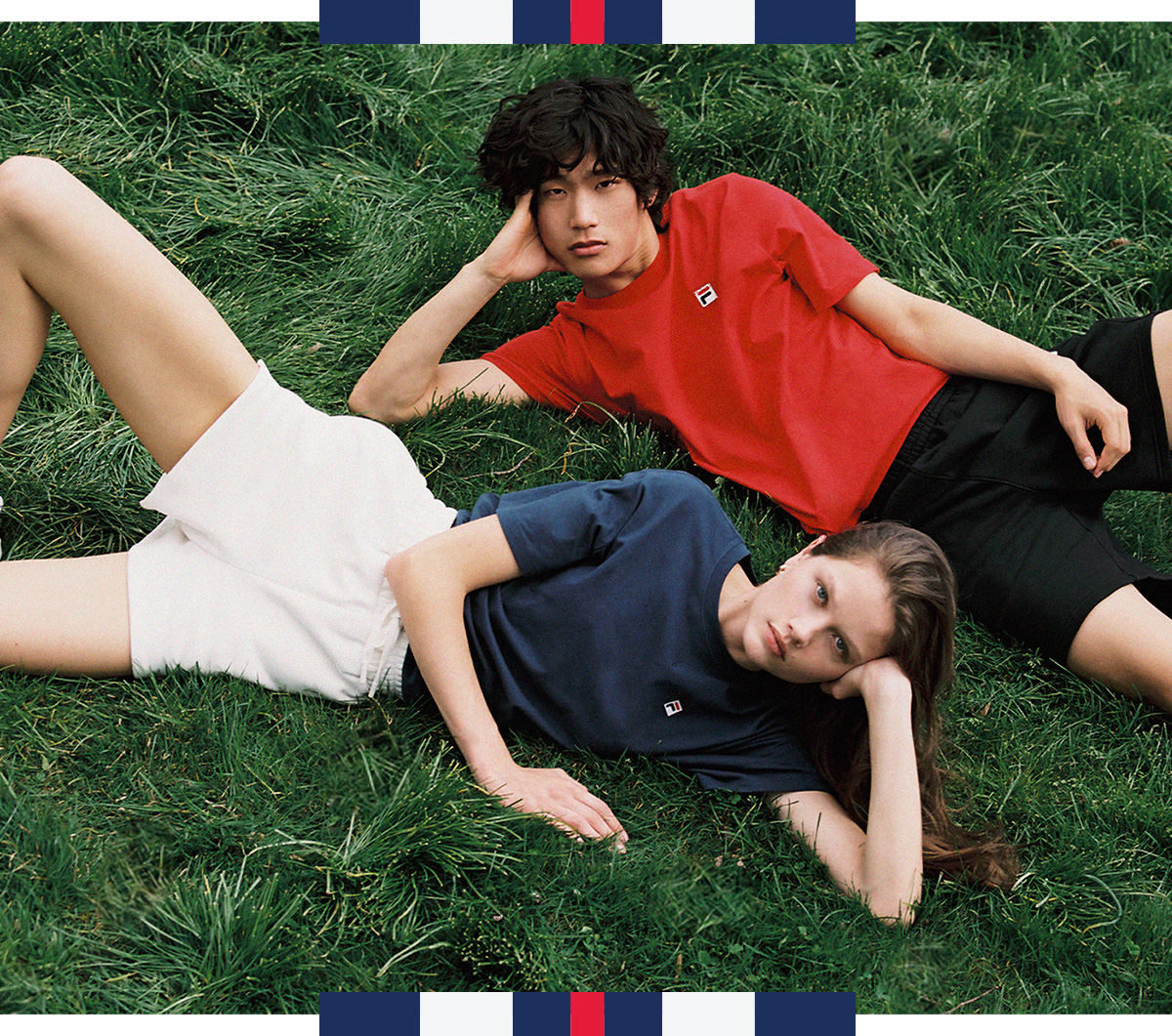 Man, wearing red shirt and black shorts, and woman, wearing navy shirt and white shorts, lying in grass.