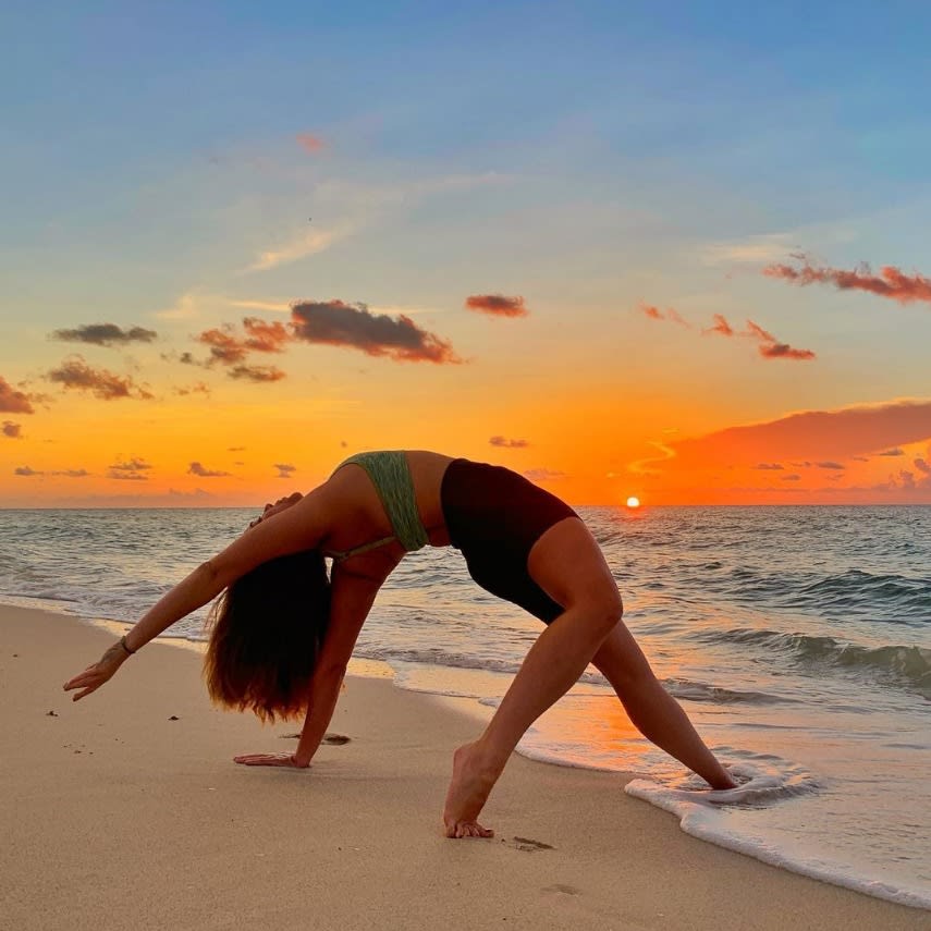 A woman doing yoga on the beach at sunset