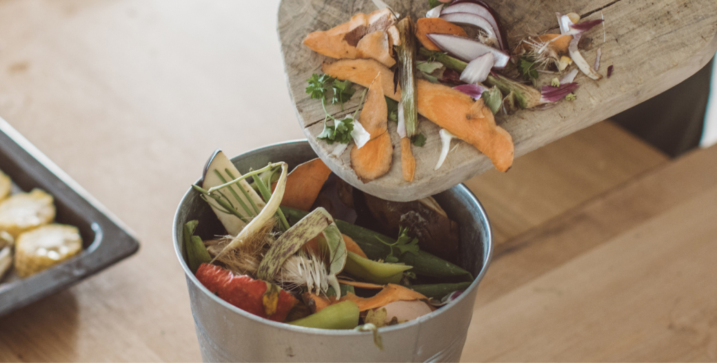 A person moving food waste from a cutting board into a bucket