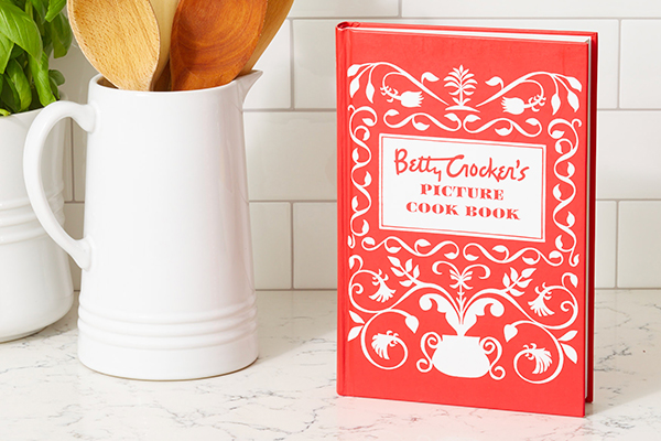 Betty Crocker's Picture Cook Book on a kitchen counter with jar of spoons