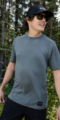 Man wearing a grey Todra while in a forest with trees behind him