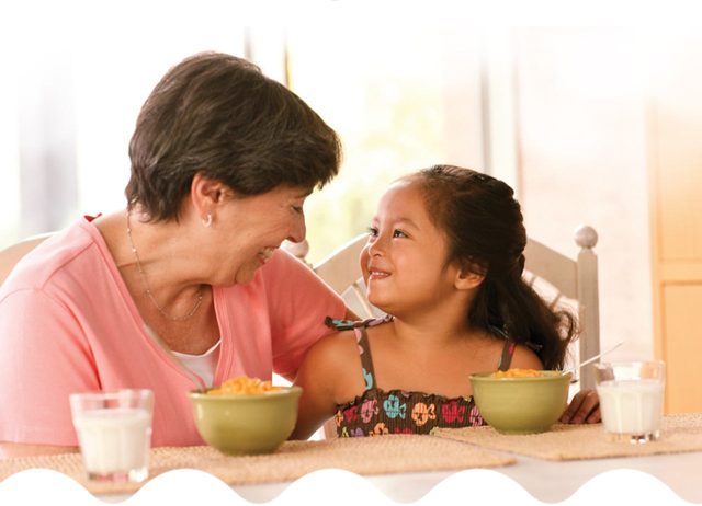 An older woman and a young girl smiling and eating breakfast together.