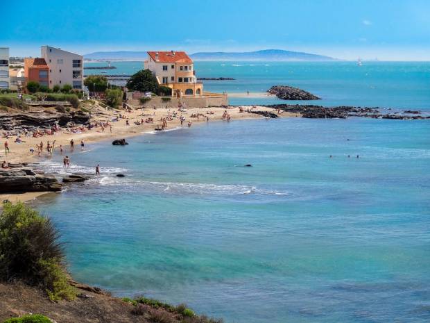 Bird's eye view of the tip of Cap d'Agde. Mixture of rocks, sunny buildings on a sea background.