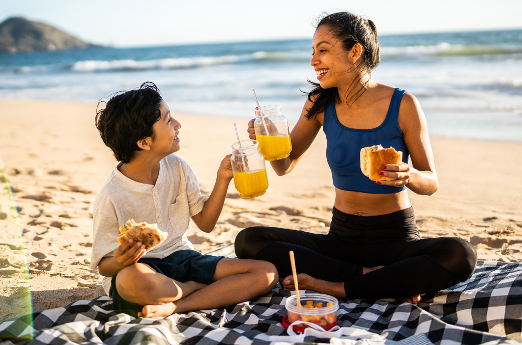 Woman and child enjoying food and a orange juice in the beach