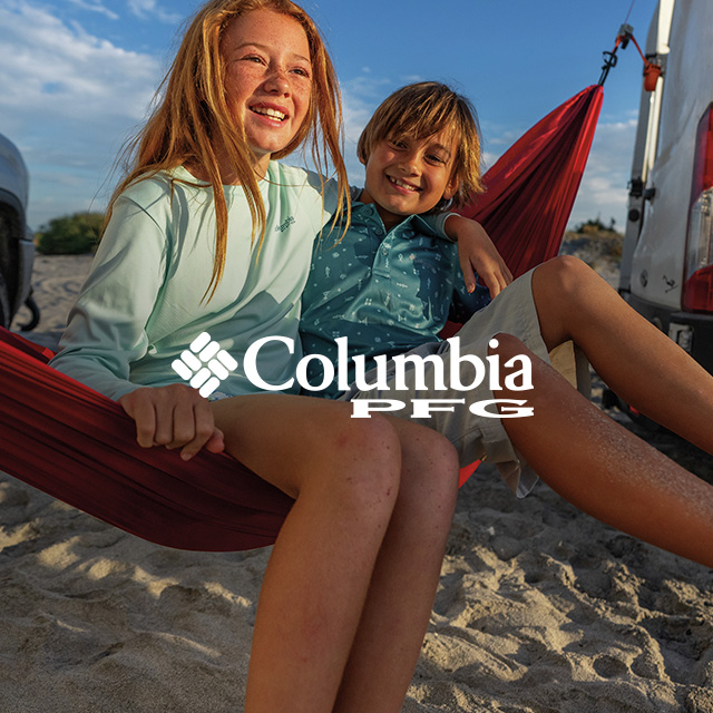 Two kids smiling in a hammock on the beach.