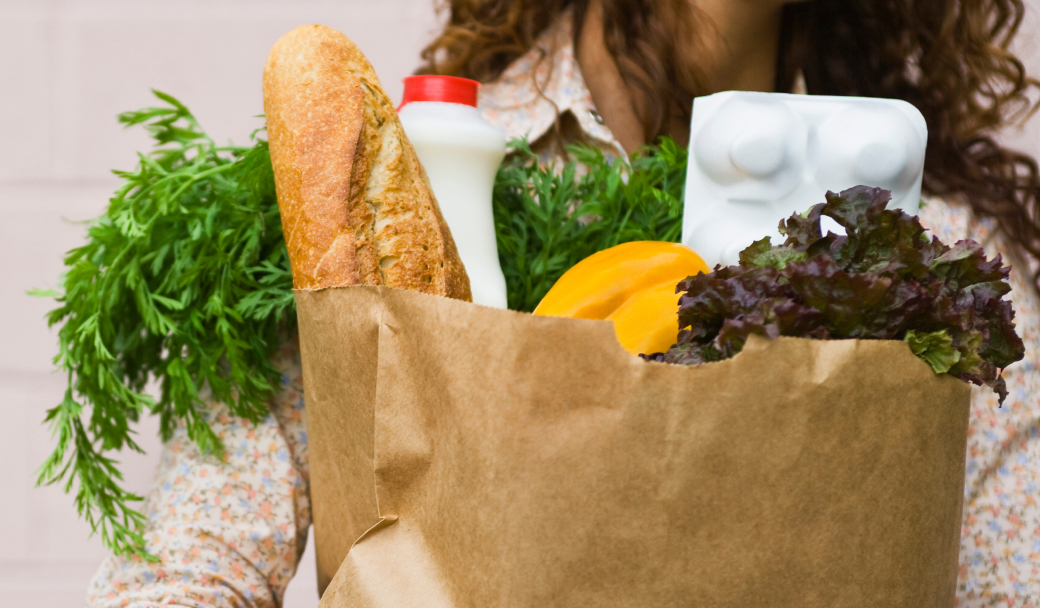 A person holding a cardboard grocery bag with different food inside