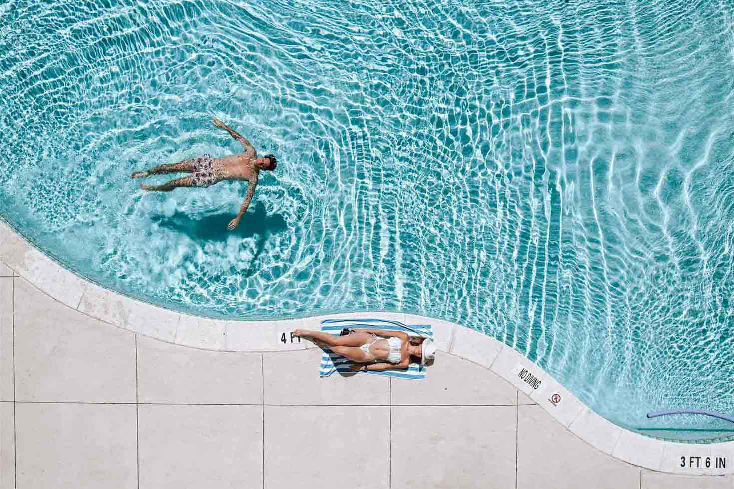 A man and woman lounge at a clear blue pool