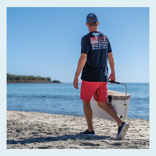 A man walking down the beach with a cooler.