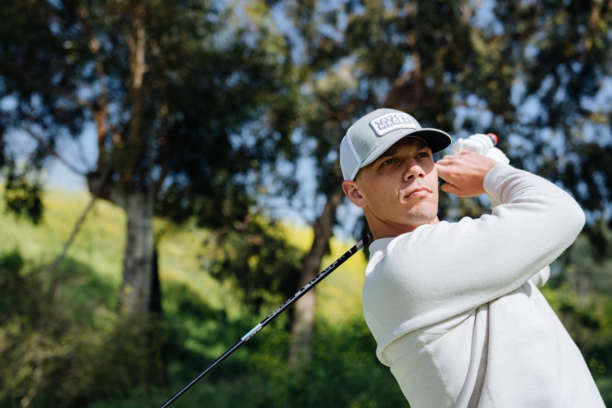 Male Golfer swinging a golf club outdoors with trees in the background, wearing the Retro TaylorMade Trucker hat in grey and white