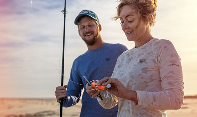 A couple in fishing gear baiting a line.